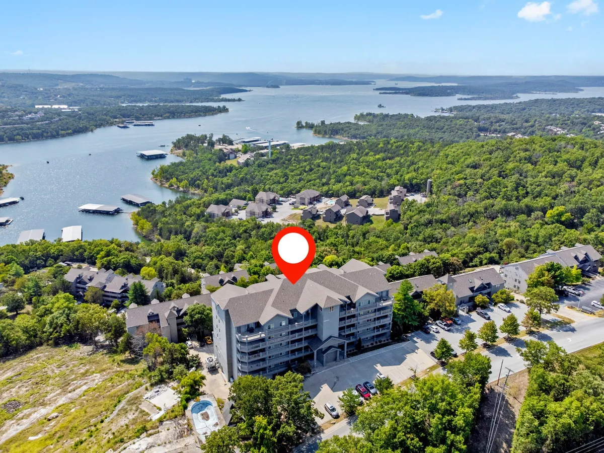 A scenic exterior view featuring a large building nestled next to a lake, bordered by verdant greenery. The tranquil water and surrounding hills evoke a sense of adventure and provide a visual cue for outdoor activities and lakeside relaxation.