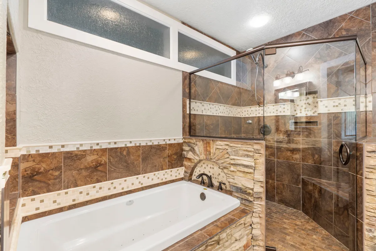 A spa-like bathroom with a luxurious bathtub, glass shower enclosure, and elegant stone wall details. The space is designed for relaxation and rejuvenation, offering an upscale bathing experience.