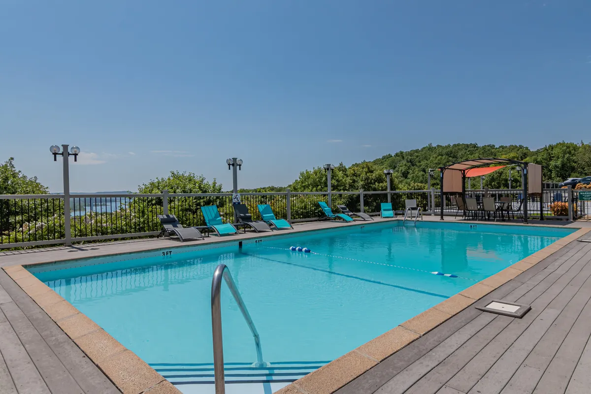 This exterior image features a sparkling swimming pool surrounded by lounge chairs and landscaped greenery. A canopy shades a seating area, and the scene is bright and cheerful, suggesting leisurely afternoons and social gatherings by the pool.