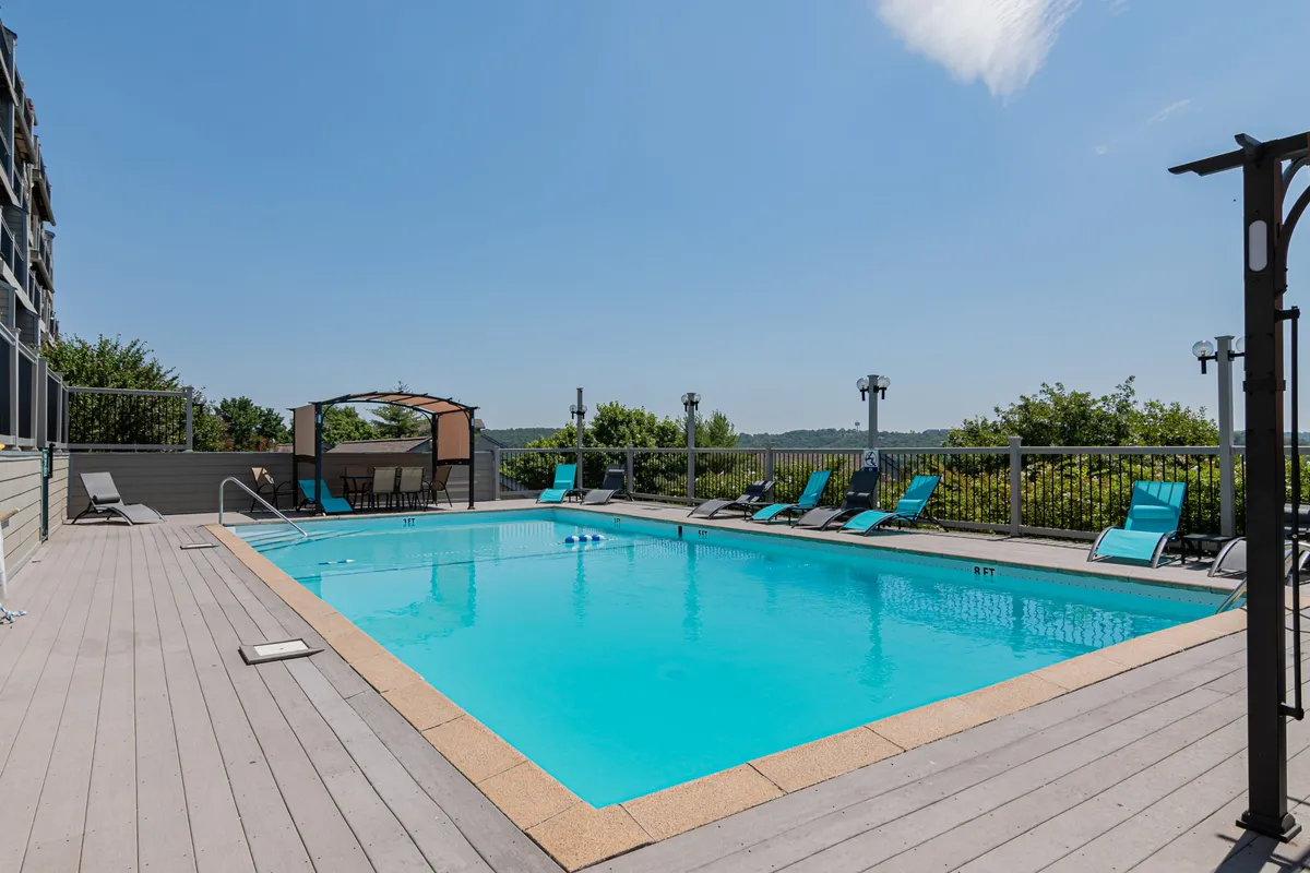 A sun-drenched outdoor swimming pool with lounge chairs and a cabana, surrounded by greenery. The atmosphere is relaxed, highlighting the resort-style amenities available to guests and offering a spot for both leisure and socialization.
