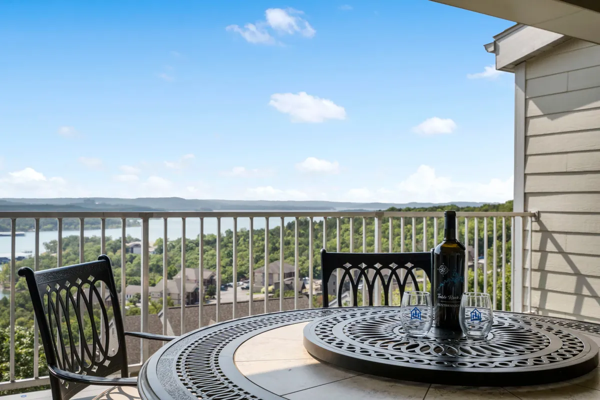 A table set with a wine bottle and glasses overlooks a panoramic vista of the lake and rolling hills. The scene exudes relaxation and sociability, inviting guests to unwind after a day of exploring local attractions, possibly while recounting their adventures.
