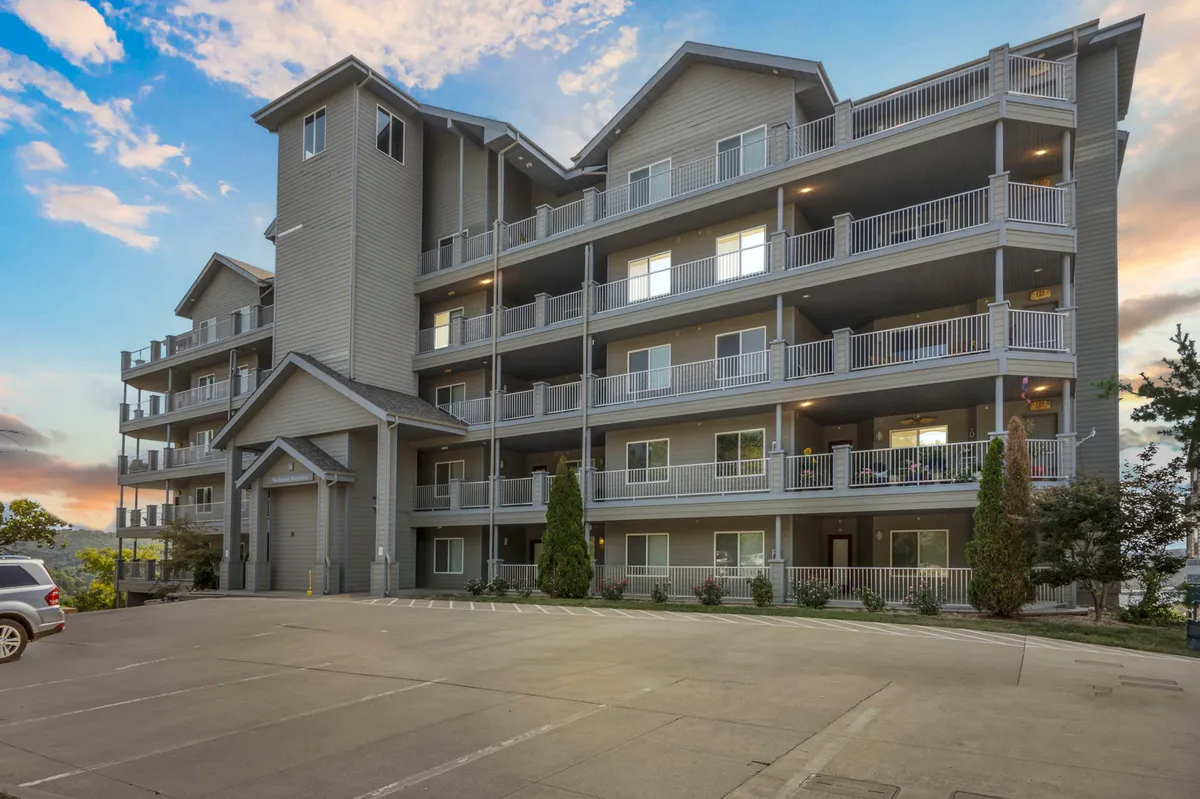 A welcoming exterior view of the condo building, featuring balconies, a landscaped entrance, and the warm glow of sunset. The image captures moments of guests relaxing outdoors and enjoying the community ambiance.
