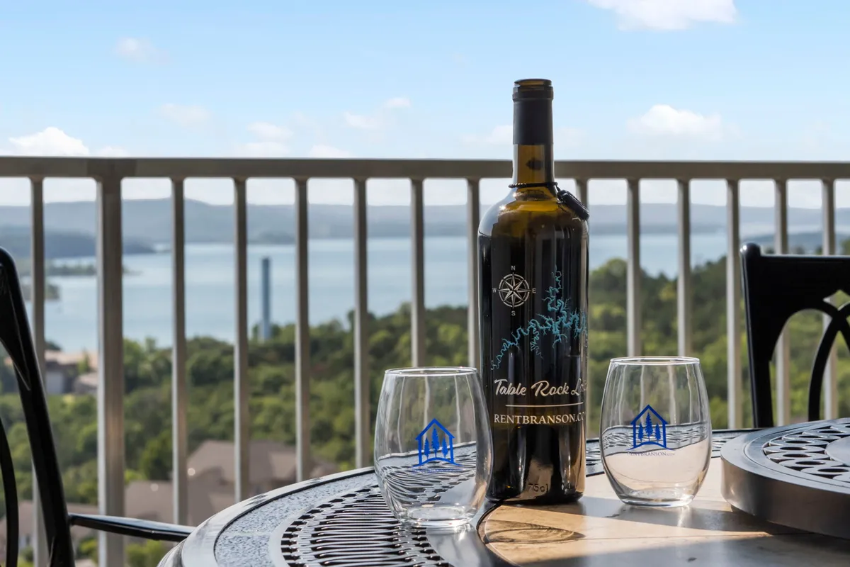 This image shows a private deck or balcony set with a wine bottle and two glasses, overlooking a stunning expanse of Table Rock Lake. The view invites relaxation, with the tranquil water and distant hills providing a breathtaking backdrop for unwinding with a drink, whether in the morning or at sunset.