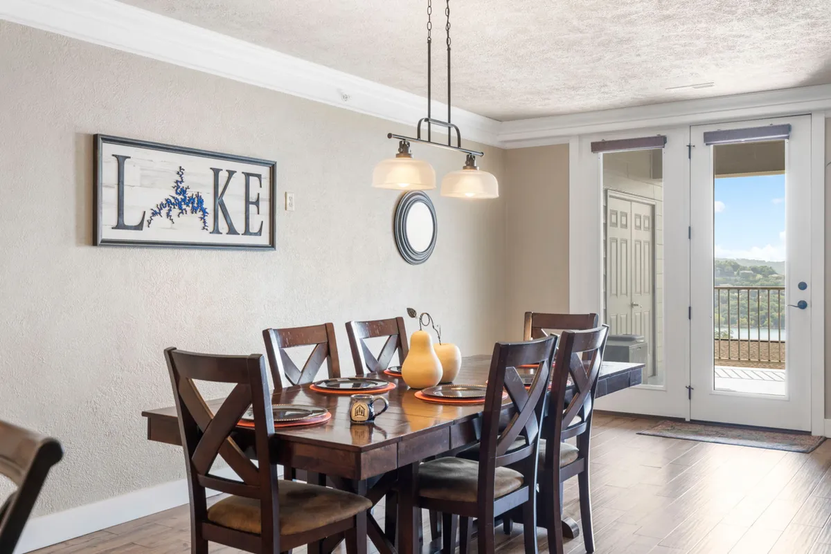 A dining area with a welcoming table, lake-themed wall art, and sliding glass doors leading outside. The table is set for a meal or gathering, and the room exudes warmth and togetherness.