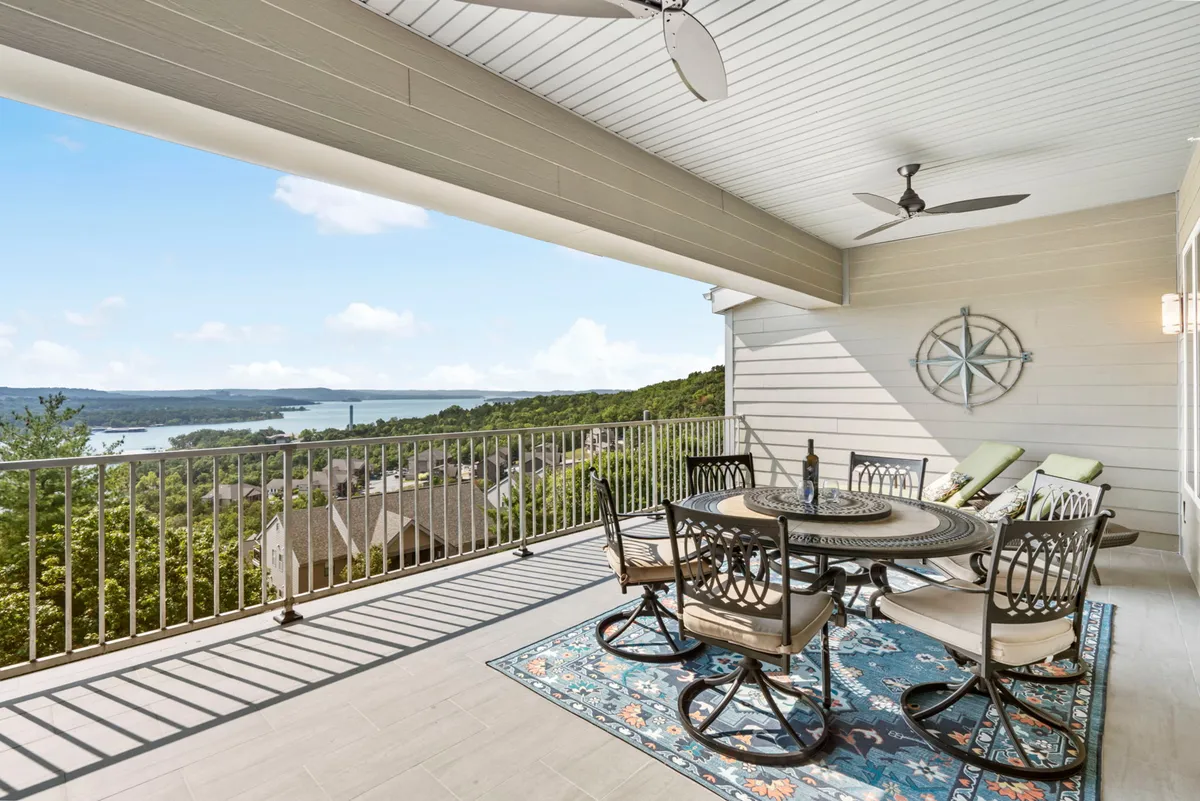 An inviting exterior deck with a dining table, decorative rug, and ceiling fans overlooking the lake. The setup is perfect for outdoor dining, relaxing, or hosting sunset gatherings, with the shimmering water visible in the background.