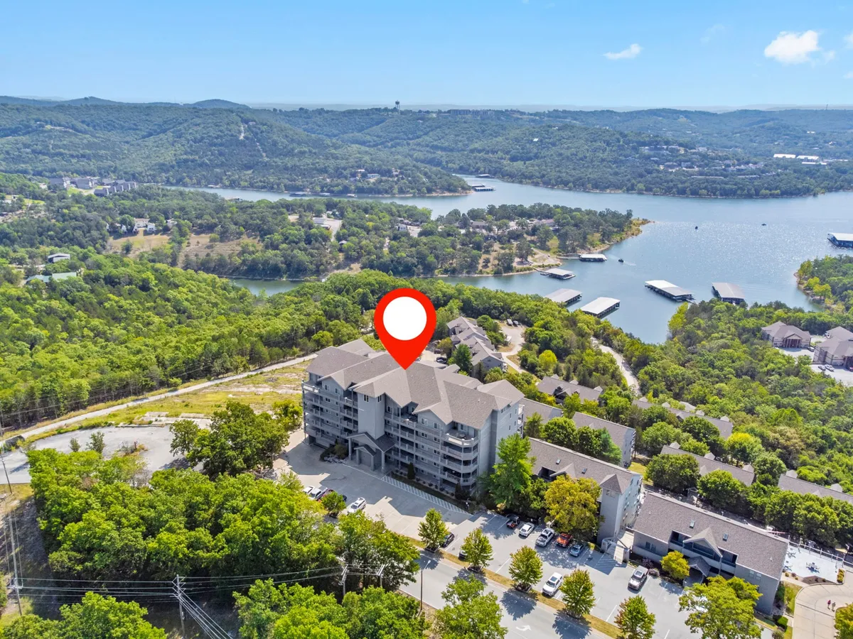 This exterior image shows the main building set against lush greenery with water visible in the background. The scene hints at recreational activities like boating and hiking, with the tranquility of lakeside living front and center.