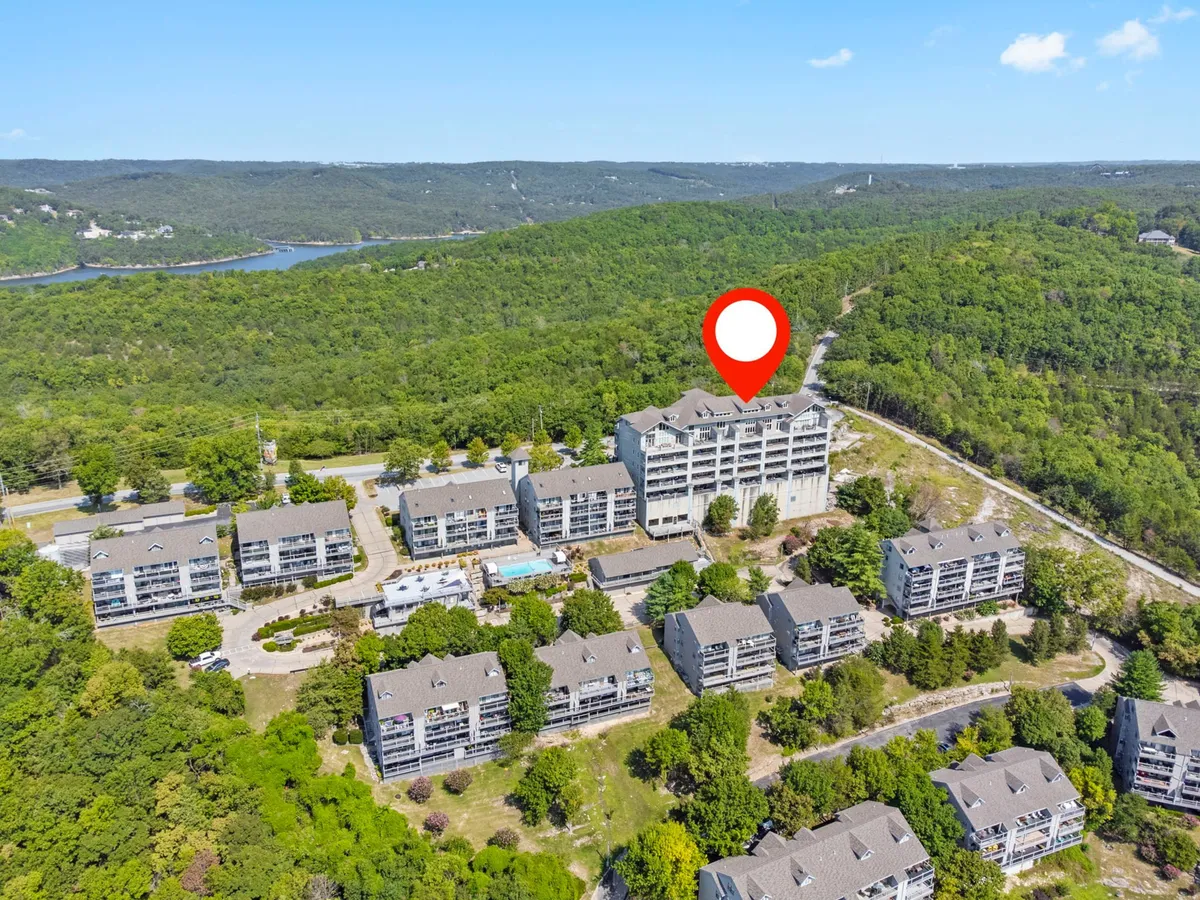 This image captures the main building with a red pin, surrounded by neighboring apartments, lush greenery, and a sparkling pool area. The setting highlights the proximity to nature and recreational amenities, while the vantage point suggests easy access to local attractions and an inviting environment for exploration.