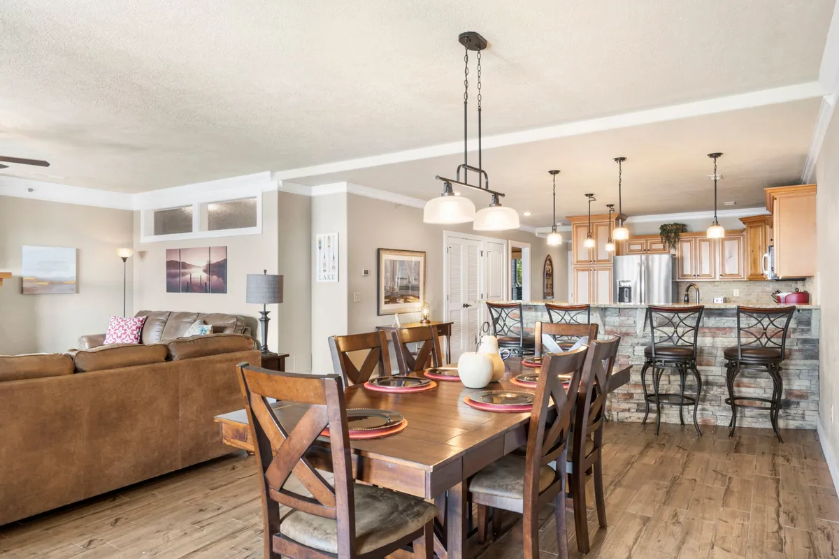 A view of the dining table, sofa, and kitchen island, all arranged for both family dinners and casual gatherings. Stylish light fixtures add warmth while the open-plan layout fosters connectivity and comfort.