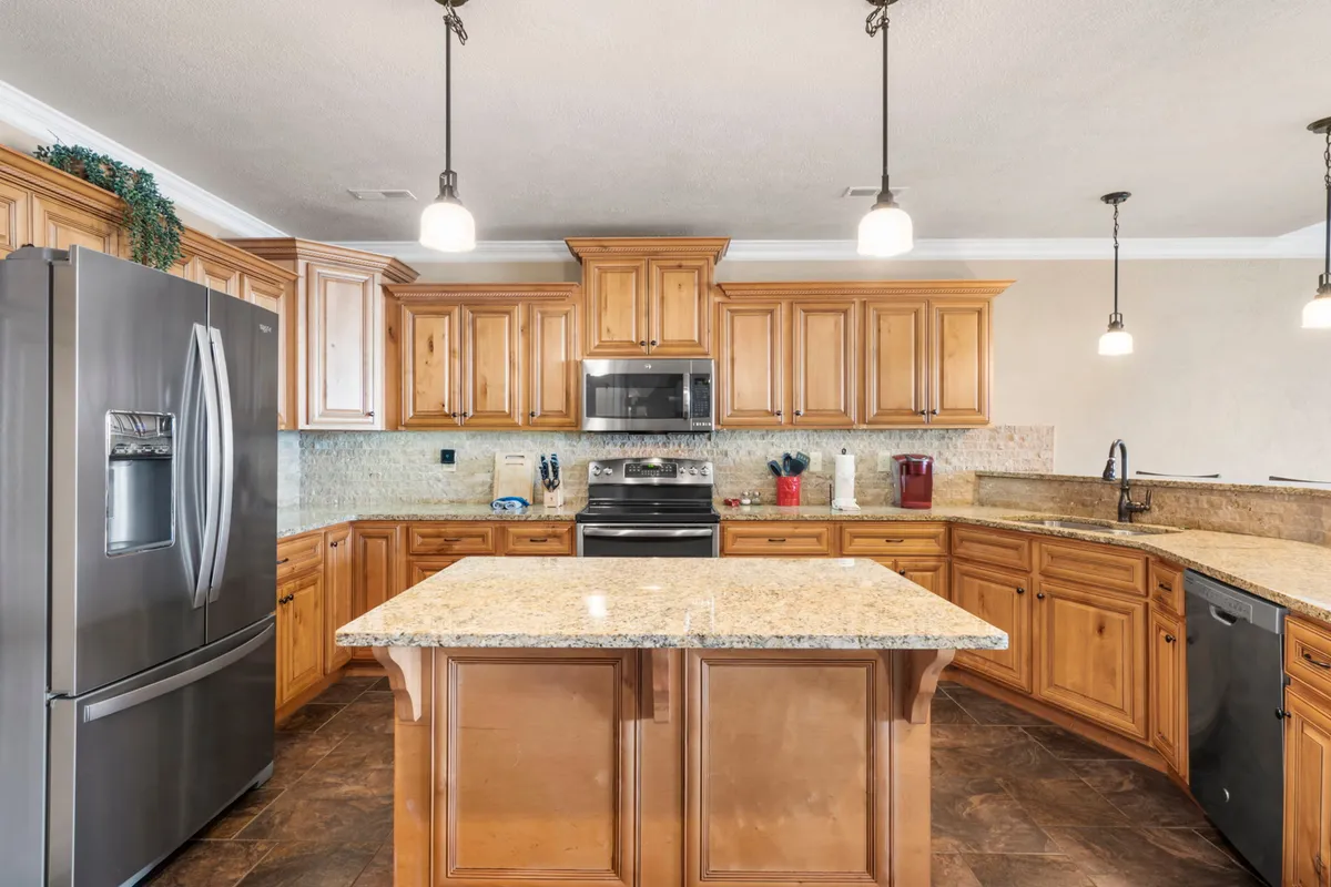 A modern kitchen with a central island, stainless steel appliances, granite countertops, and warm wooden cabinetry. The scene hints at an inviting, spacious environment perfect for preparing meals and entertaining guests.