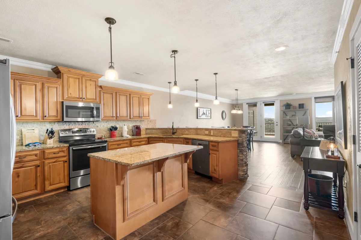 An open-concept kitchen featuring an island countertop, stainless steel appliances, and large windows offering a view of the lake. The inviting atmosphere suggests a space ideal for both meal prep and socializing, with natural light flooding in.